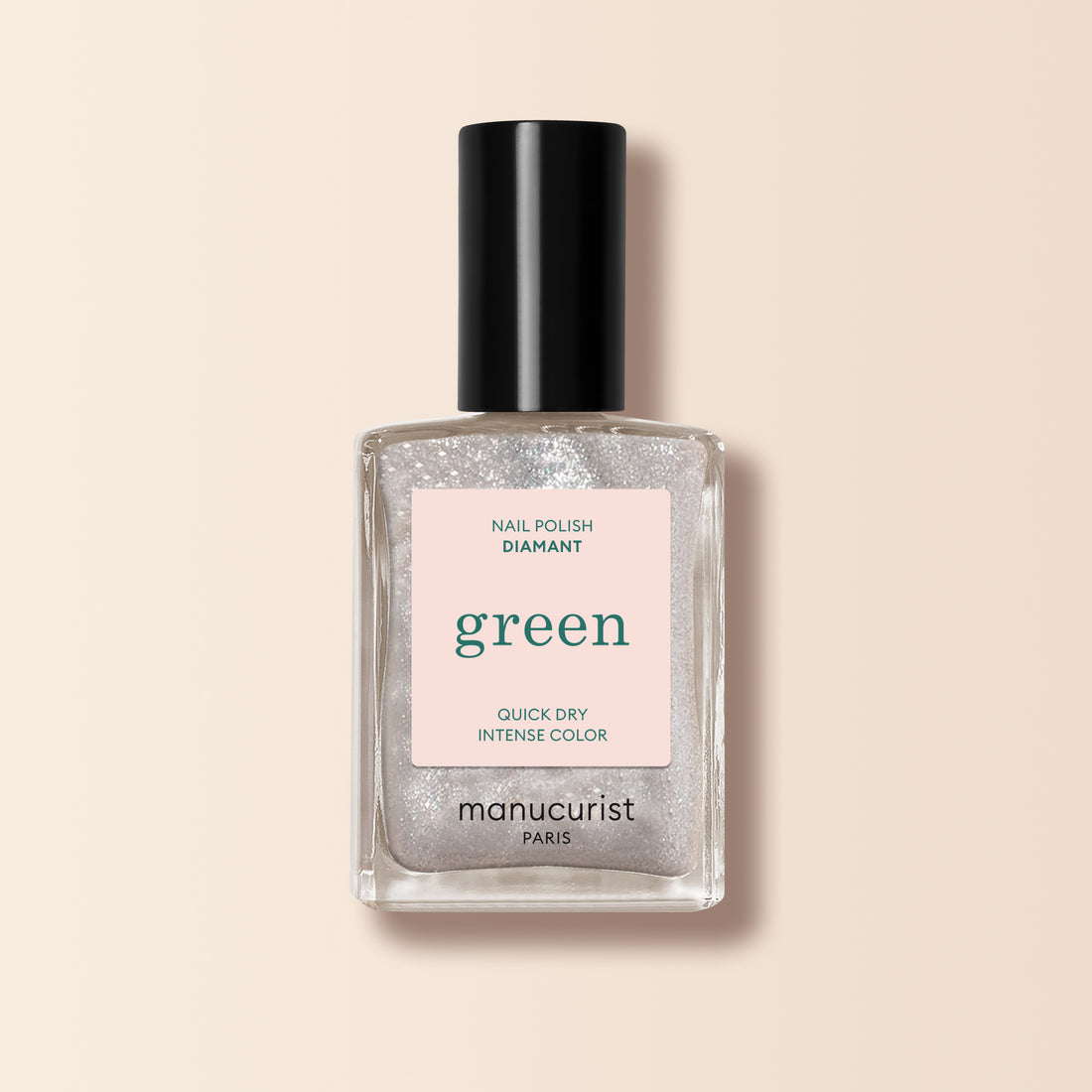 Un flacon de vernis à ongles Manucurist Diamant de la gamme Green, révélant une teinte pailletée argentée transparente, un bouchon noir et une étiquette rose pâle, présenté sur un fond beige clair.