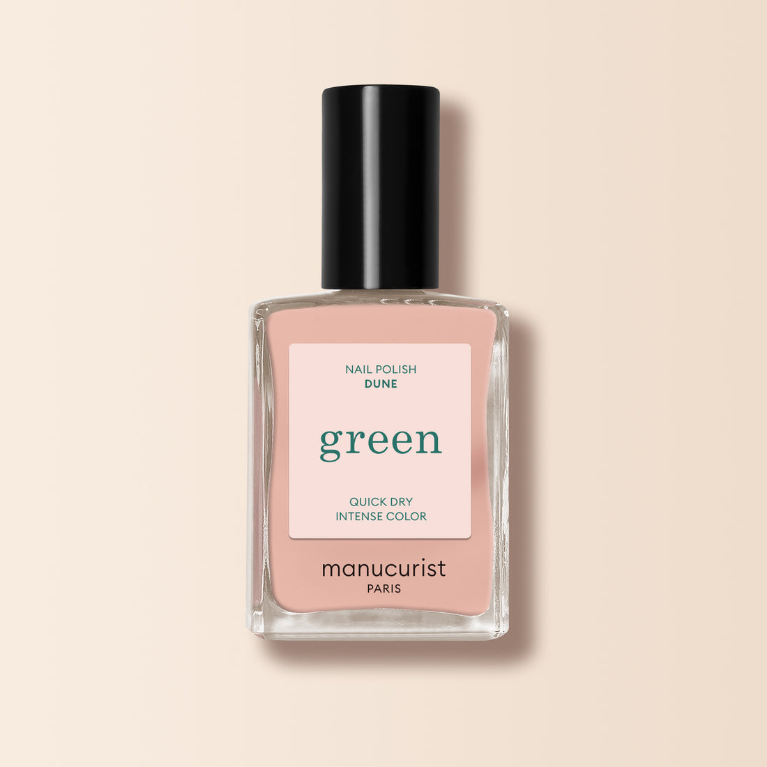 Un flacon de vernis à ongles Manucurist Dune avec un bouchon noir, portant la mention "green,", est présenté sur un fond beige pâle. Cette teinte rose nude douce révèle de subtils sous-tons orangés.