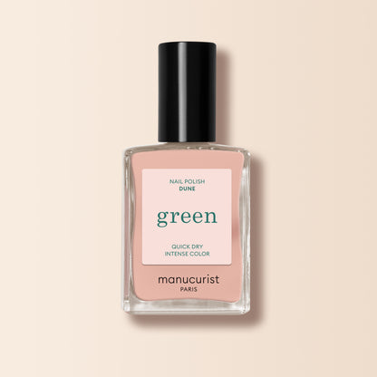 A bottle of Manucurist Dune nail polish with a black cap, labeled "green," is shown against a pale beige background. The soft nude pink shade features subtle orange undertones.