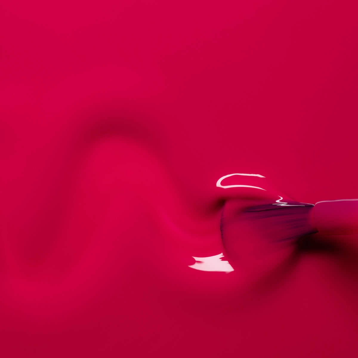 A close-up of a brush spreading Manucurist Fuchsia gel polish in a wavy line on a smooth surface, with glossy reflections highlighting the vibrant pink color.