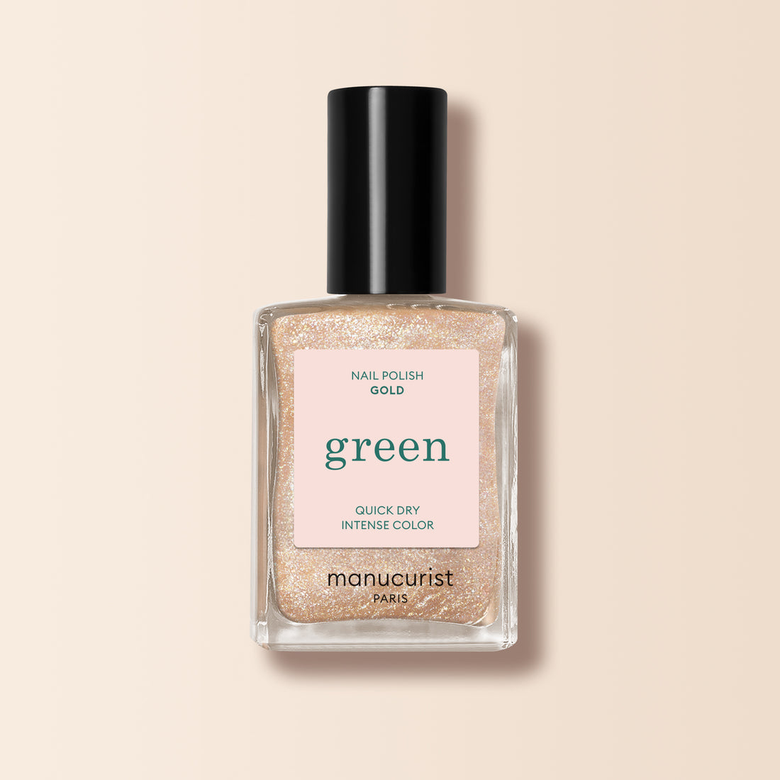 A bottle of Manucurist Gold nail polish from the Green range, with a black cap and a pink label stating "green," "nail polish gold," and "quick dry intense color," displayed on a beige background.