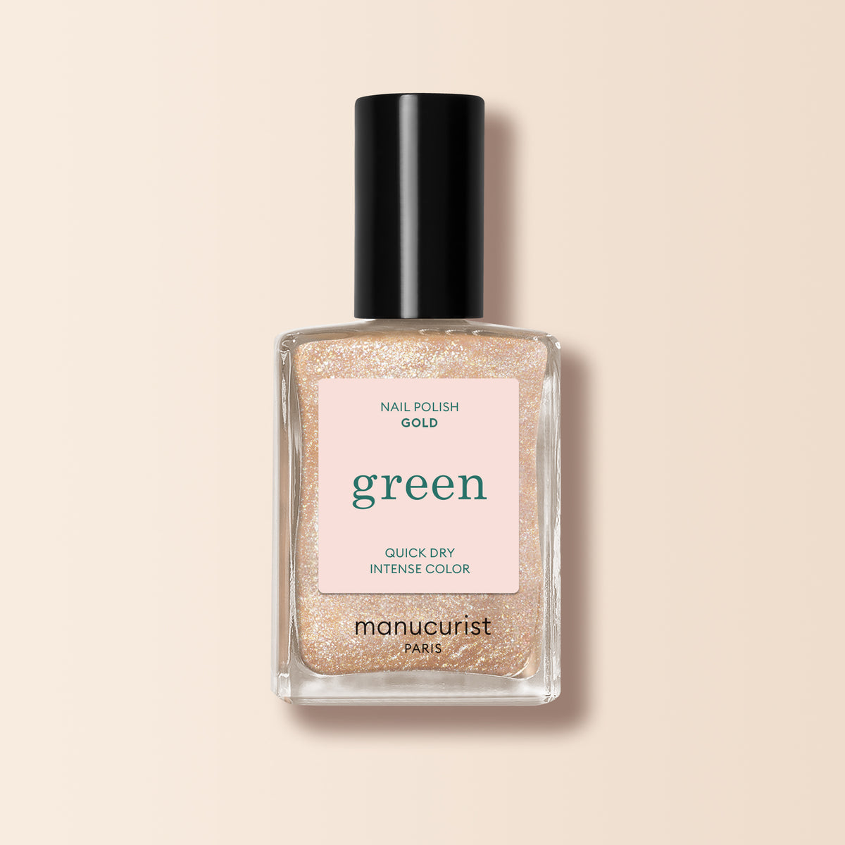 Un flacon de vernis à ongles Manucurist Gold de la gamme Green, avec un bouchon noir et une étiquette rose indiquant "green," "nail polish gold," et "quick dry intense color," présenté sur un fond beige.