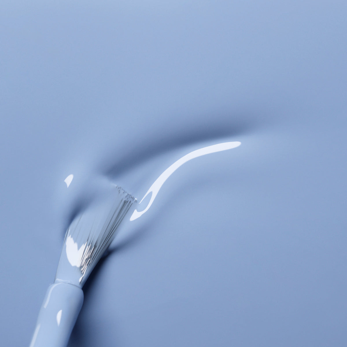 A white nail brush glides through Manucurist’s Lilas, a glossy pastel blue gel polish, leaving a textured curved streak on a smooth surface.