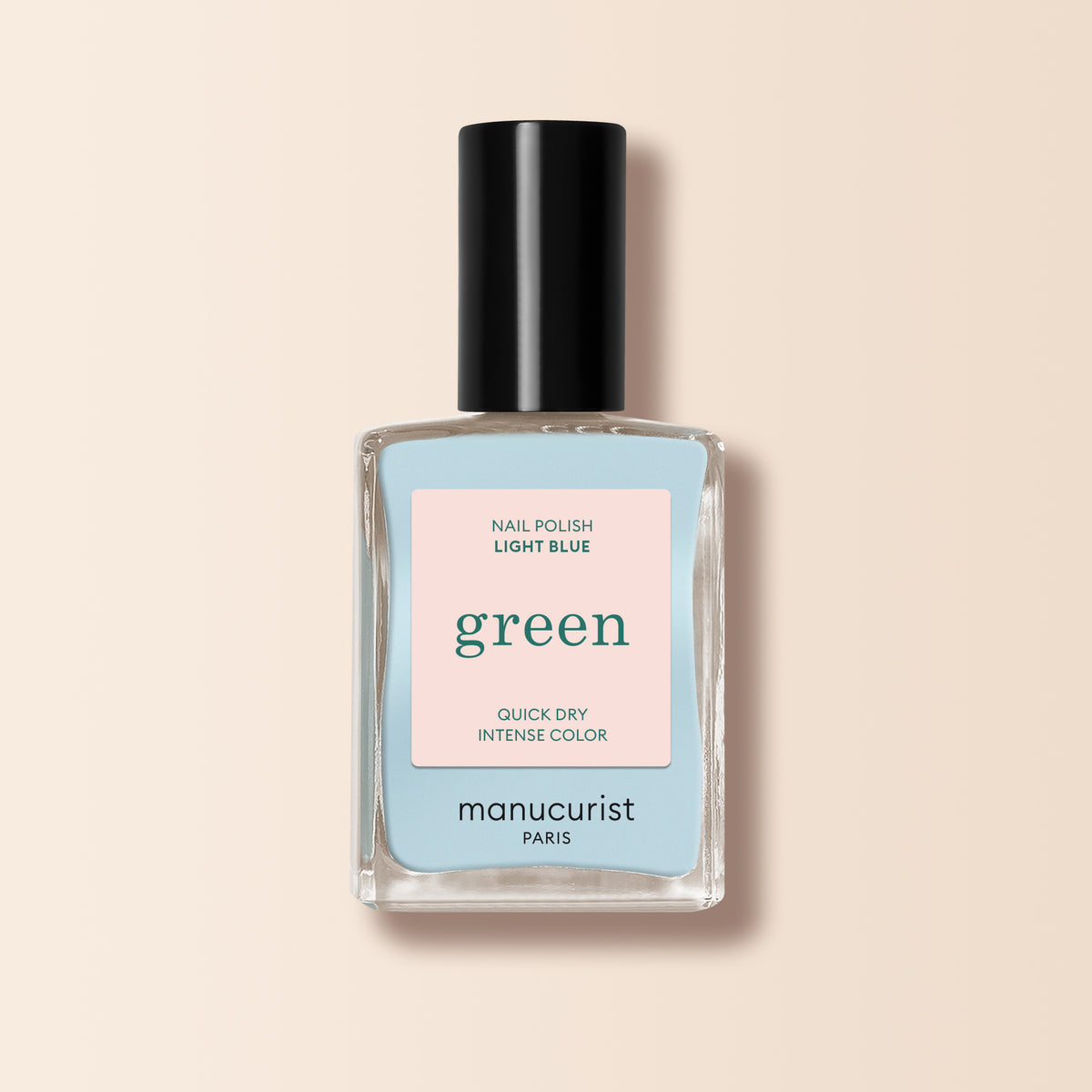 Un flacon de vernis à ongles Manucurist Light Blue de la gamme Green™, avec un bouchon noir et une étiquette « green quick dry intense color », est présenté sur un fond beige.