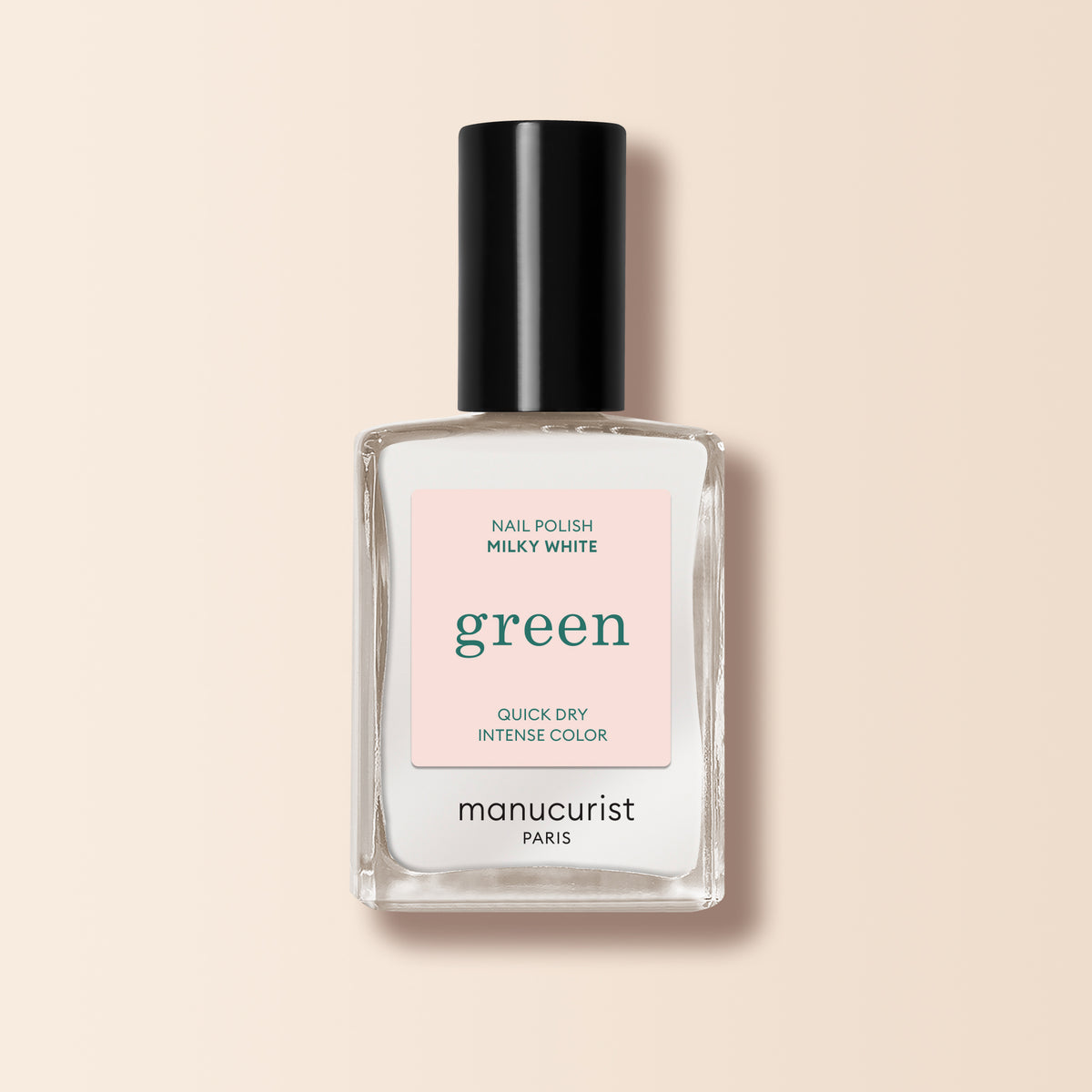 Un flacon en verre transparent de vernis à ongles Milky White de Manucurist, avec un bouchon noir, se tient debout sur un fond beige pâle.