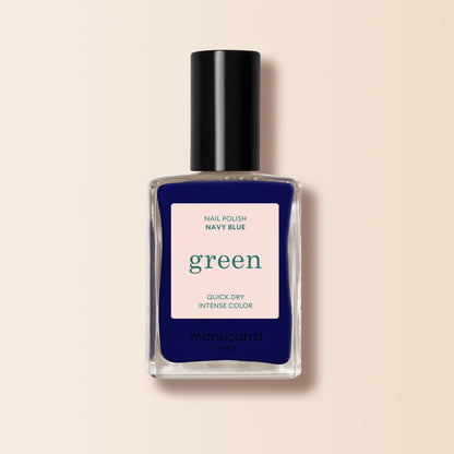 Un flacon de vernis à ongles Navy Blue de Manucurist de la gamme Green™, avec un bouchon noir. L’étiquette indique Nail Polish Navy Blue, Quick Dry Intense Color et manucurist Paris. Le fond est beige doux.