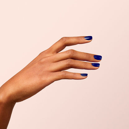 Une main à la peau mate est présentée sur un fond beige clair, les doigts légèrement écartés pour dévoiler des ongles impeccablement vernis avec la teinte Navy Blue de Manucurist.