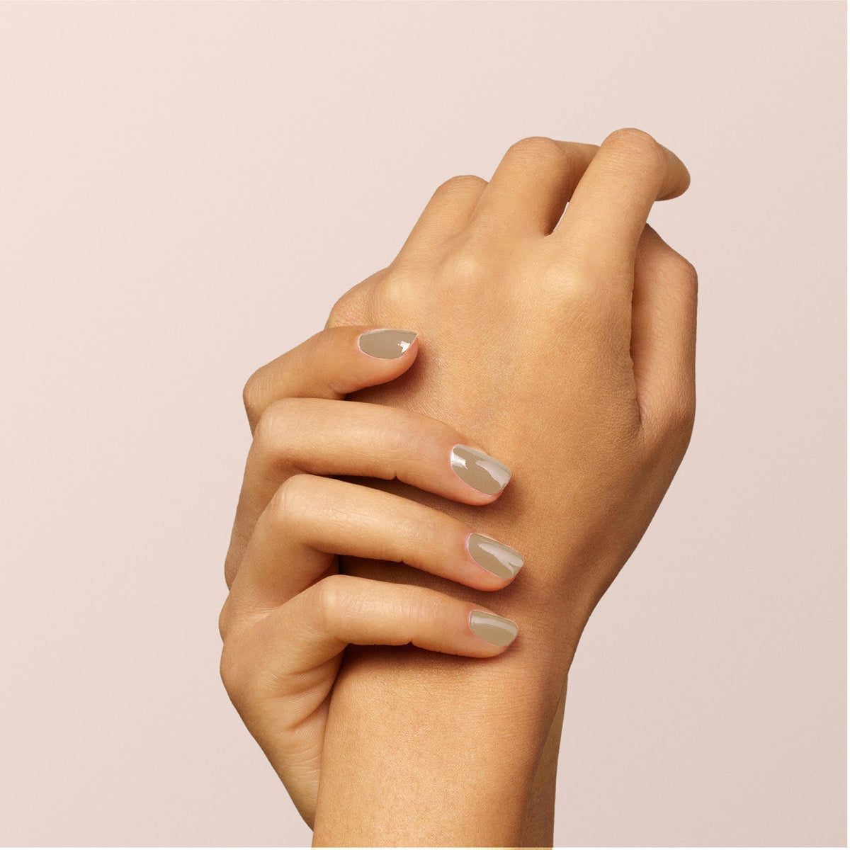 A close-up of two hands gently holding each other, displaying neatly manicured nails painted in the glossy Orme shade by Manucurist against a light beige background.