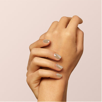 A close-up of two hands gently holding each other, displaying neatly manicured nails painted in the glossy Orme shade by Manucurist against a light beige background.