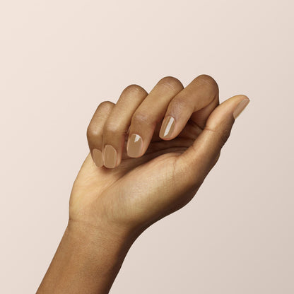 A hand with medium brown skin is shown against a light beige background. The neatly manicured nails are painted with "Orme," a glossy shade from the Manucurist Green™ range. The fingers are gently curled inward in a relaxed pose.