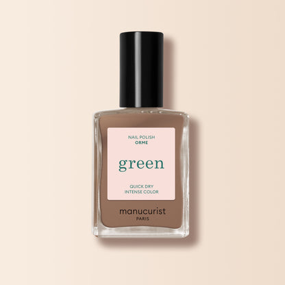 A bottle of Manucurist Orme nail polish from the Green™ range, in a café au lait light brown shade with quick-dry, intense color, black cap, and minimalist label displayed on a beige background.