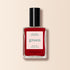 A bottle of Manucurist Pomegranate nail polish, featuring a red shade with a black cap and white label displaying green and red text, is shown against a light beige background.