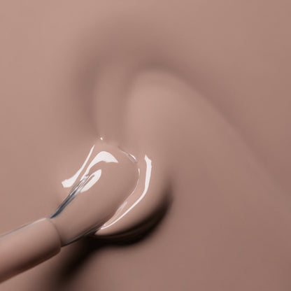 A close-up of a nail polish brush spreading Manucurist’s Dove Beige from the Green™ range on a smooth surface, forming a glossy pastel swirl.