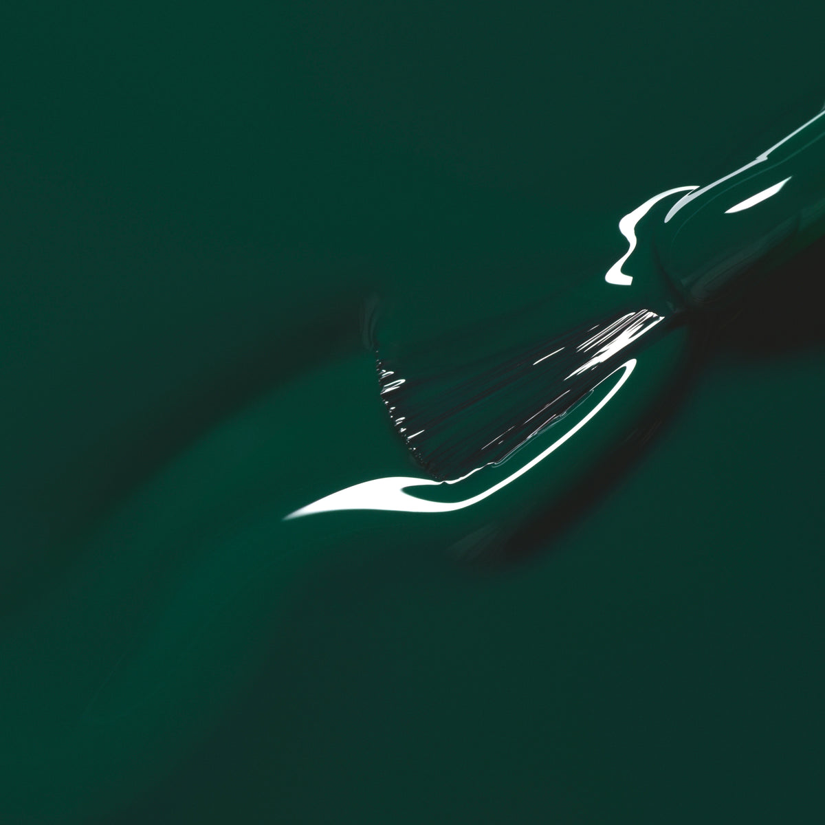 Gros plan sur un pinceau qui étale le vernis Emerald de Manucurist, un vert forêt profond et brillant, tandis que la lumière se reflète sur sa surface encore humide.