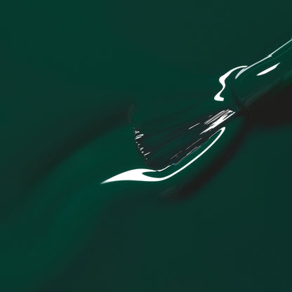 Gros plan sur un pinceau qui étale le vernis Emerald de Manucurist, un vert forêt profond et brillant, tandis que la lumière se reflète sur sa surface encore humide.
