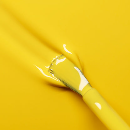 Un pinceau enduit de vernis Gold Button de Manucurist se fond parfaitement sur une surface jaune vif, créant un effet lisse et artistique.