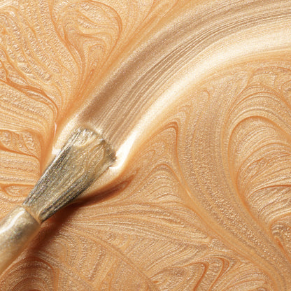 A close-up of a brush spreading shimmering, metallic gold paint with swirling patterns—evoking the brilliance of Manucurist&