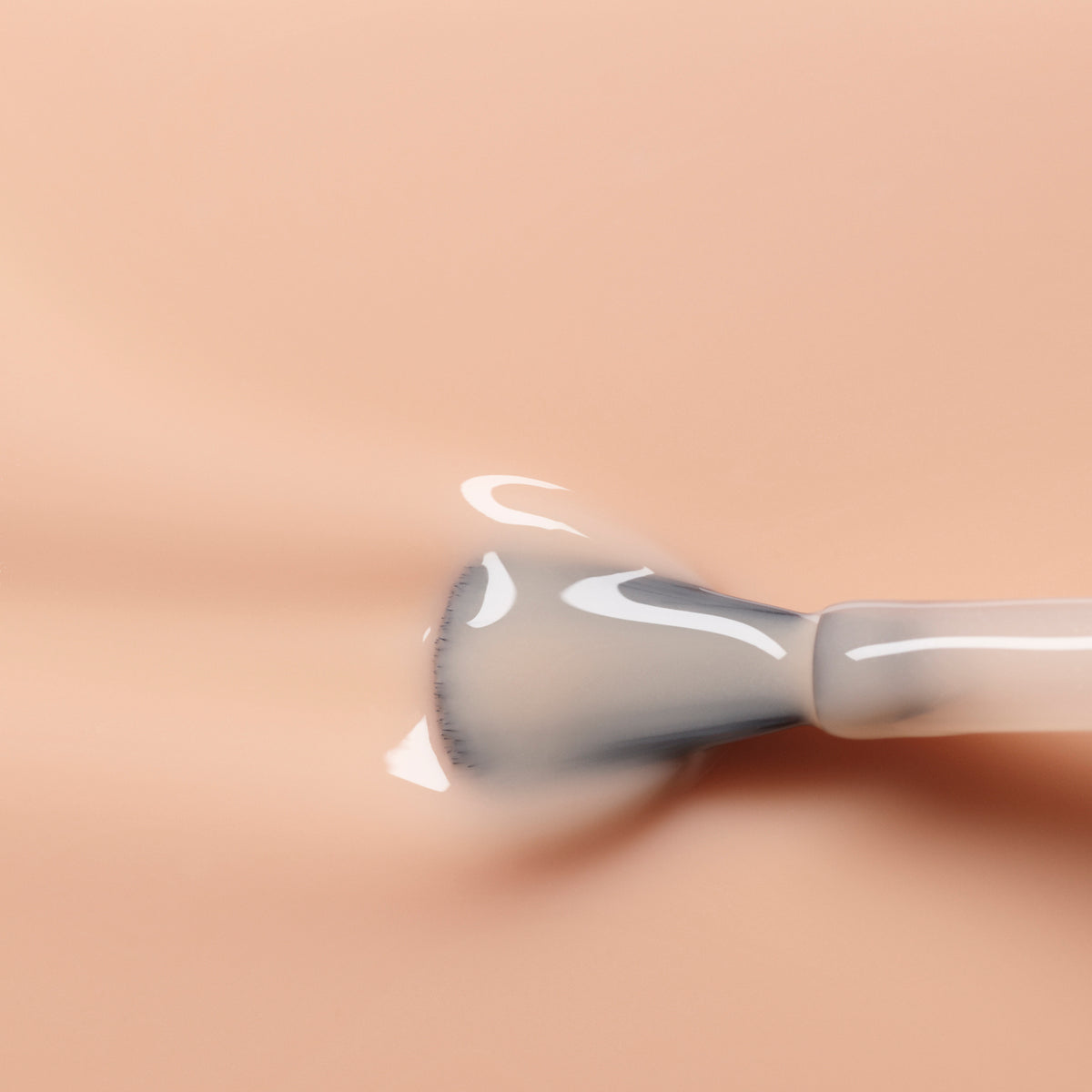 A close-up of a Manucurist nail polish brush applying glossy Beige polish on a smooth surface. The brush is partially coated with the shiny nude shade, creating a beautifully reflective effect.