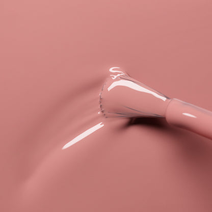 A close-up of a nail polish brush applying Manucurist Old Rose, a smooth, glossy antique powder pink shade, onto a matching pink surface.