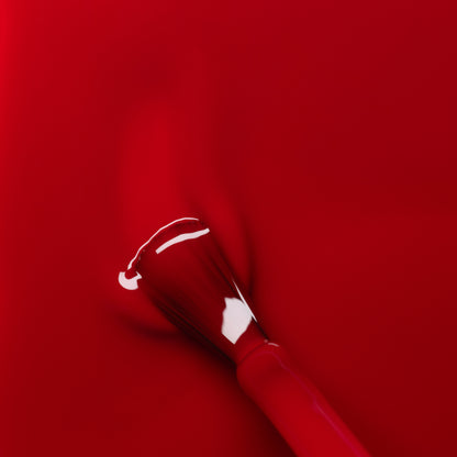 A close-up of the Manucurist Red Cherry nail polish brush spreading vibrant red color on a glossy surface, creating smooth, even strokes with a shiny finish.