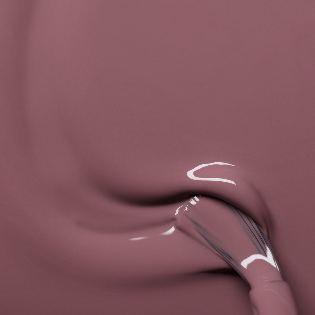 A close-up of a brush applying Manucurist’s Rose Mountbatten gel polish, creating smooth, shiny swirls in the thick, glossy pinky taupe formula.