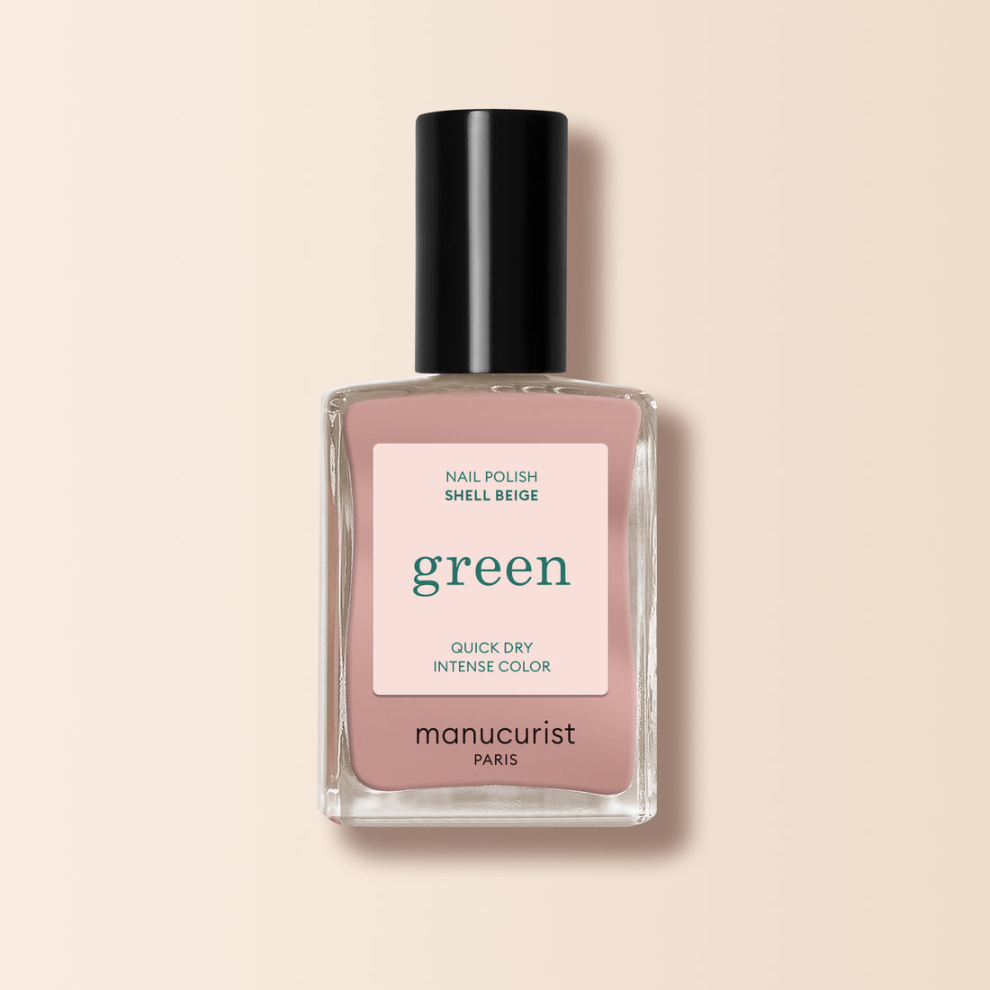 Un flacon de vernis à ongles Shell Beige de Manucurist, issu de la gamme Green™, avec un bouchon noir, un flacon en verre transparent et une étiquette beige-rose indiquant « green, quick dry intense color », sur fond beige clair.