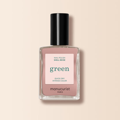 A bottle of Manucurist Shell Beige nail polish from the Green™ range, with a black cap, clear glass bottle, and a beige-pink label reading “green, quick dry intense color,” set against a light beige background.