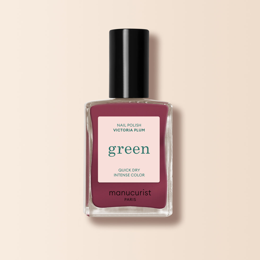 Un flacon de vernis à ongles Manucurist Victoria Plum, présentant une teinte prune profonde, un bouchon noir et une étiquette blanche avec du texte vert et rose, est présenté sur un fond beige clair.