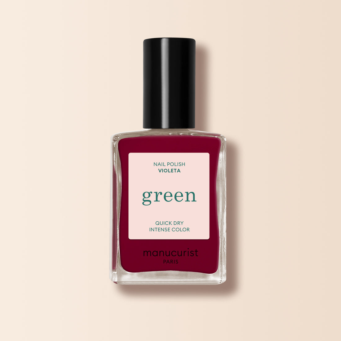 Un flacon transparent de vernis à ongles Manucurist Violeta avec un capuchon noir, issu de la gamme Green™, Quick Dry Intense Color. La teinte bordeaux violet profond se détache sur un fond beige doux.