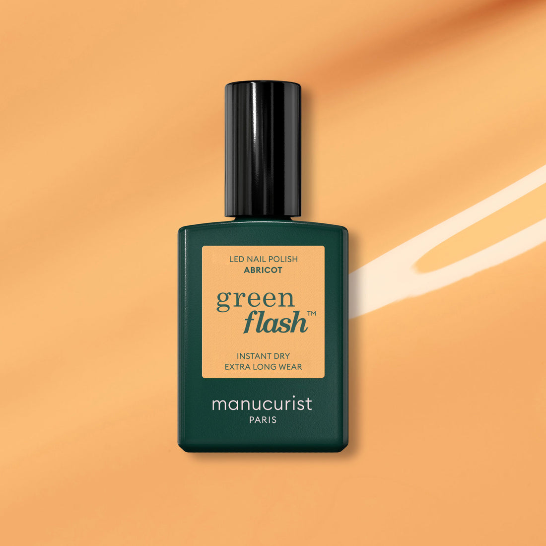 Un flacon de vernis gel Manucurist Abricot est présenté sur un fond orange avec une touche de pinceau blanche.