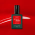 A bottle of Manucurist Anémone gel polish stands out on a bold red background with a white brushstroke. This light red shade from Manucurist Paris pops with vibrant color and shine.