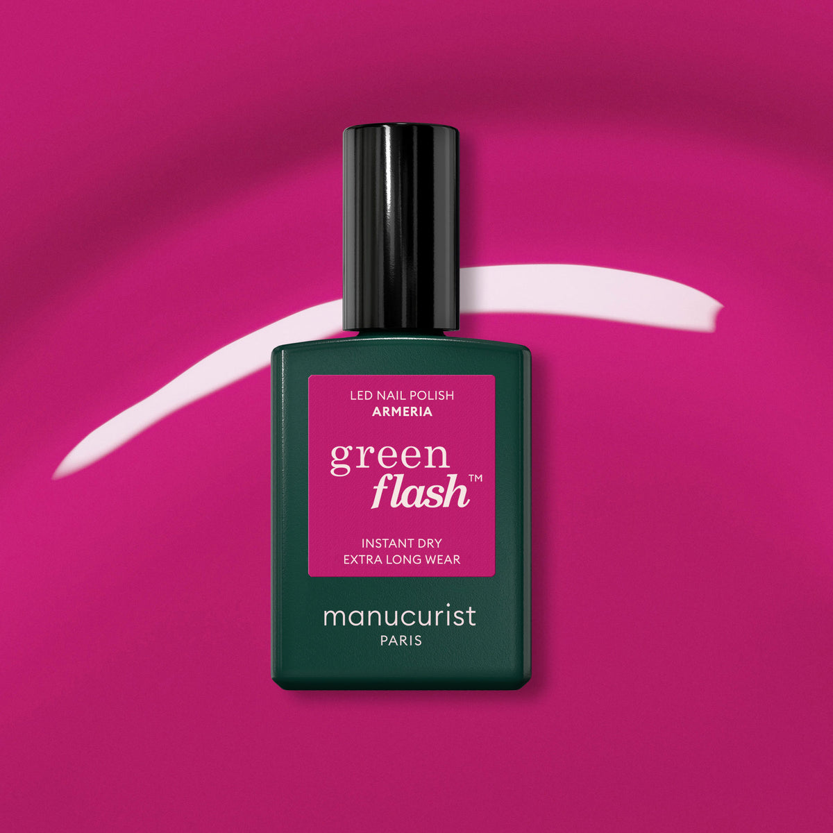 A bottle of Manucurist Armeria rests on a vibrant pink background with a curved mauve streak behind it. The dark green bottle features a black cap and a bright pink label.