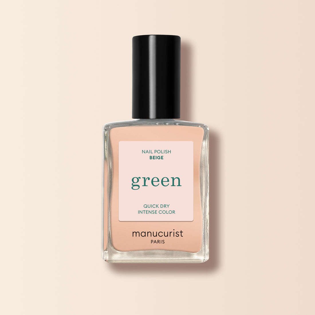 A bottle of Manucurist Beige nail polish with a black cap, labeled “green” and “quick dry intense color,” is shown against a light beige background.