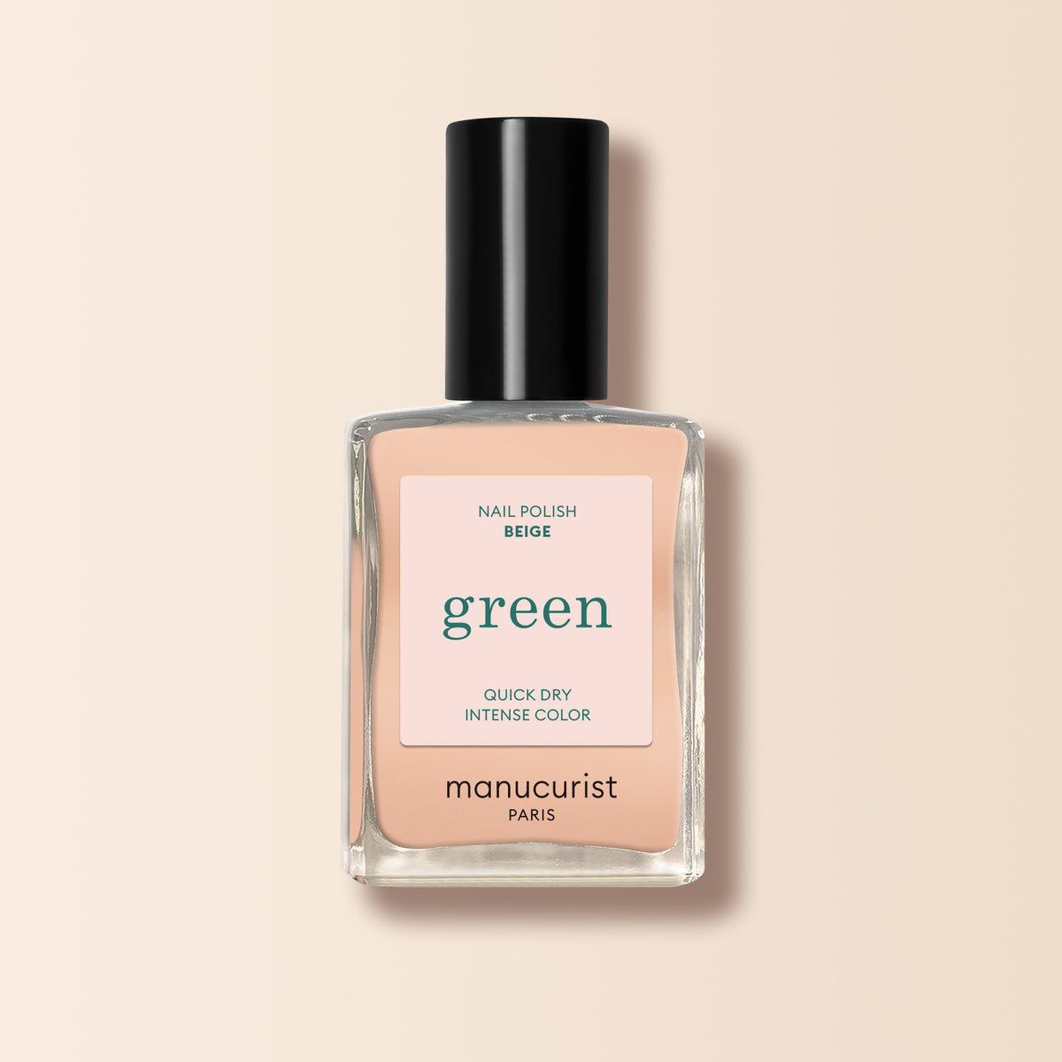 A bottle of Manucurist Beige nail polish with a black cap, labeled “green” and “quick dry intense color,” is shown against a light beige background.
