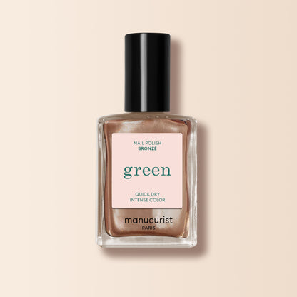 A bottle of Manucurist Bronzé nail polish in a bronze-copper shade with a black cap, set on a light beige background. The label highlights Quick Dry Intense Color.
