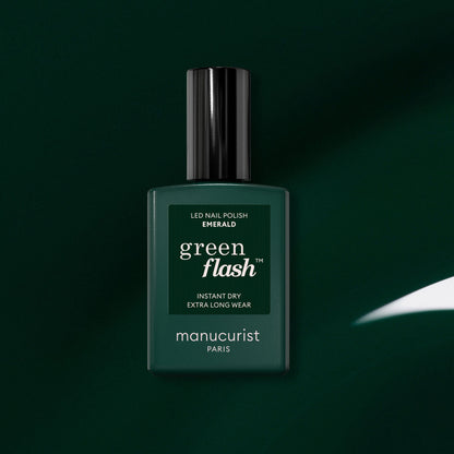 Un flacon de vernis semi-permanent LED Green Flash de Manucurist en teinte Emerald est placé au centre d’un fond vert foncé. Les mentions « Instant Dry » et « Extra Long Wear » figurent sur l’étiquette et soulignent l’allure riche et raffinée de ce vernis inspiré d’une pierre précieuse.