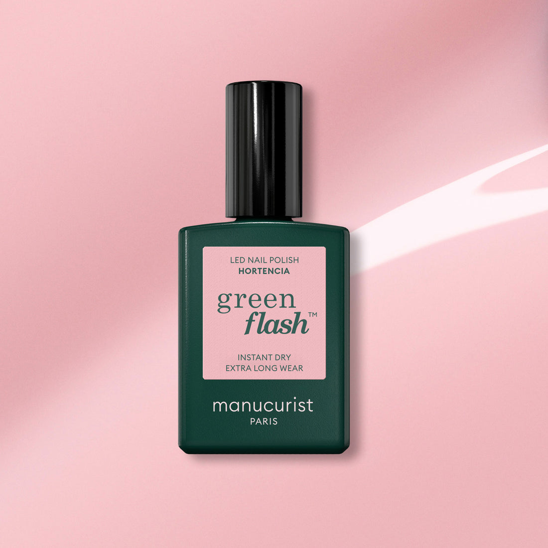 A bottle of Manucurist gel polish in the shade Hortencia rests on a pink background, showing its label “Instant dry, extra long wear.”.