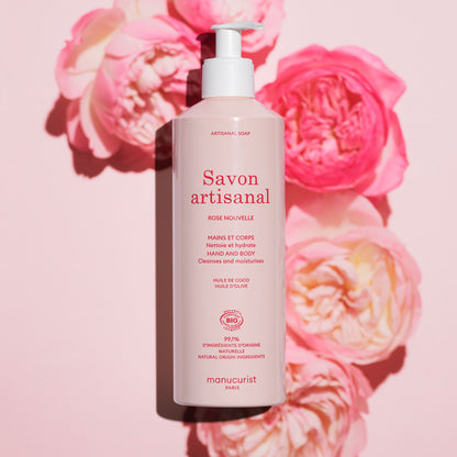 A pink bottle of Manucurist Organic Rose Hand  Body Wash - Cosmos Organic rests on a pink background with roses, its label noting a delicate rose scent and natural ingredients for luxurious hand and body care.