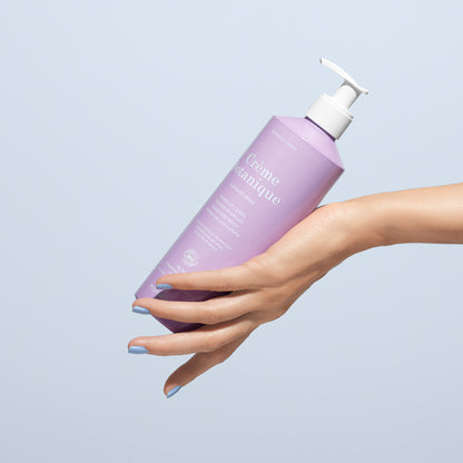 Une main aux ongles peints en bleu tient un flacon lavande de crème pour les mains et le corps Soothing Lavender Hand Body Cream - Cosmos Organic de Manucurist, doté d&