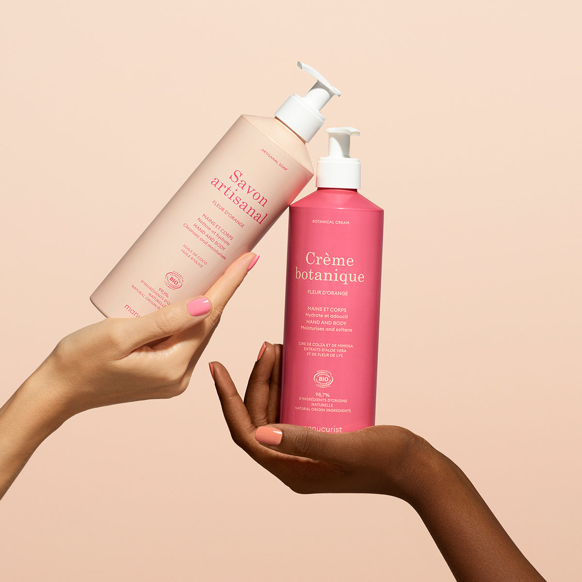 Two hands hold up Manucurist’s Orange Blossom Botanical Cream  Artisan Soap Duo - Cosmos Organic against a light peach background: the left holds the artisan soap, while the right displays the bright pink botanical cream.
