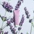 Un tube rose de Crème Mains Lavande Quotidienne Manucurist - Cosmos Organic est centré sur un fond clair avec des brins de lavande, projetant de douces ombres. Cette crème mains bio offre un parfum de lavande frais et apaisant.