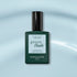 A bottle of Manucurist Light Blue Green Flash gel polish, with a dark green cap, sits on a soft blue background. The label highlights instant dry and extra long wear for this pastel sky blue shade.