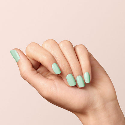 A hand with light skin tone is shown against a pale background. The nails are neatly manicured and painted with Mint nail polish from the Manucurist Green™ range, while the fingers are slightly curled inward.