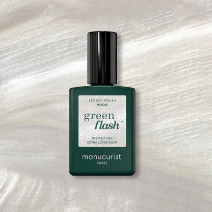 A bottle of Manucurist Moon gel polish rests on a shimmery marble background, its dark green design and white label highlighted by pearly white accents beneath.