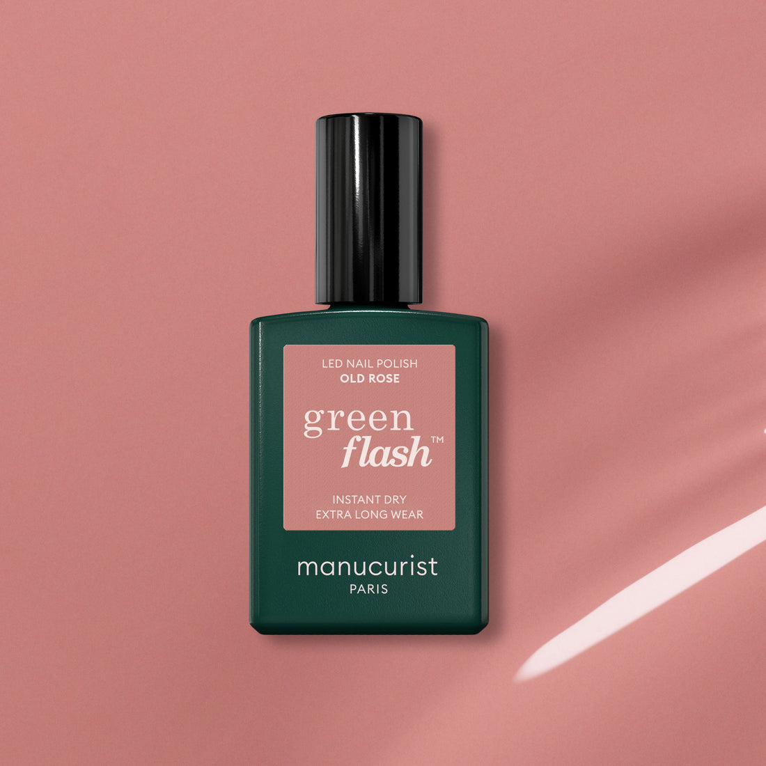 A bottle of Manucurist Old Rose, a beautiful antique pink polish, sits on a pink surface casting a soft shadow. The bottle has a dark green base and black cap.