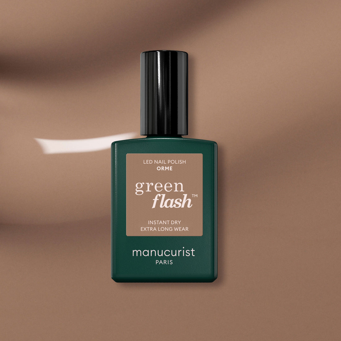Un flacon de vernis gel Orme de Manucurist, avec son étiquette beige et son bouchon noir, est posé sur une surface marron brillante. La teinte Orme signée Manucurist revisite le vernis gel classique en version écoresponsable.