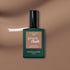 A bottle of Manucurist Orme gel polish, featuring a beige label and black cap, rests on a glossy brown surface. The Orme shade by Manucurist offers an eco-friendly update to classic gel polish.