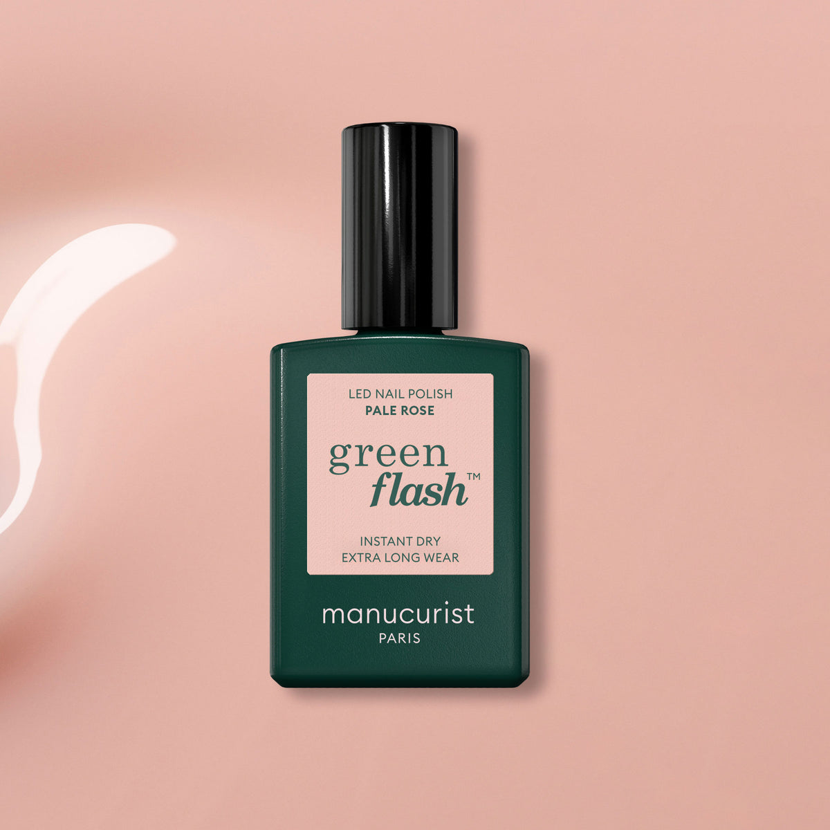 A bottle of Manucurist Pale Rose gel polish rests on a glossy light pink surface, with a shiny curved streak nearby that accentuates its soft, sheer rose shade.