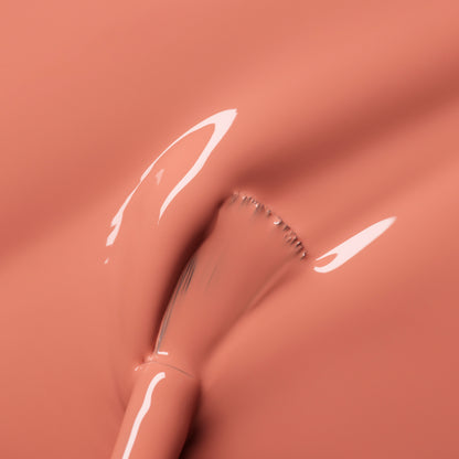 A close-up shows a brush spreading Manucurist Peach nail polish, creating smooth, shiny streaks of peachy orange tint across the liquid surface.