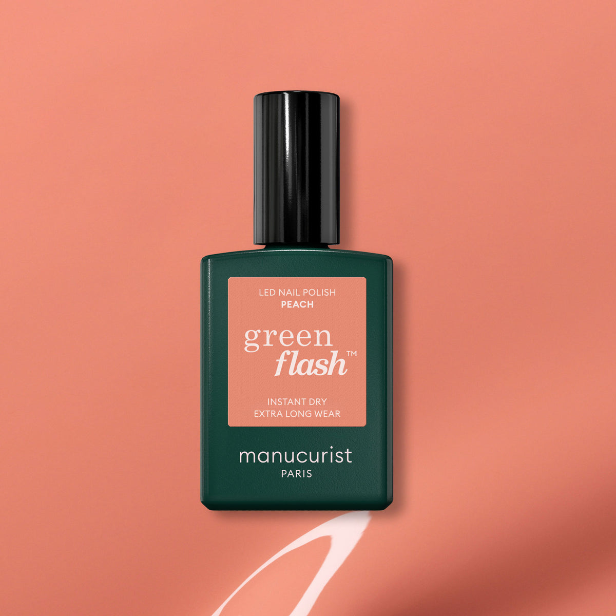 A bottle of Manucurist Green Flash gel polish in Peach rests on a peach background with a painted white swoosh underneath. The label highlights instant dry and extra long wear, making it an ideal summer tint.